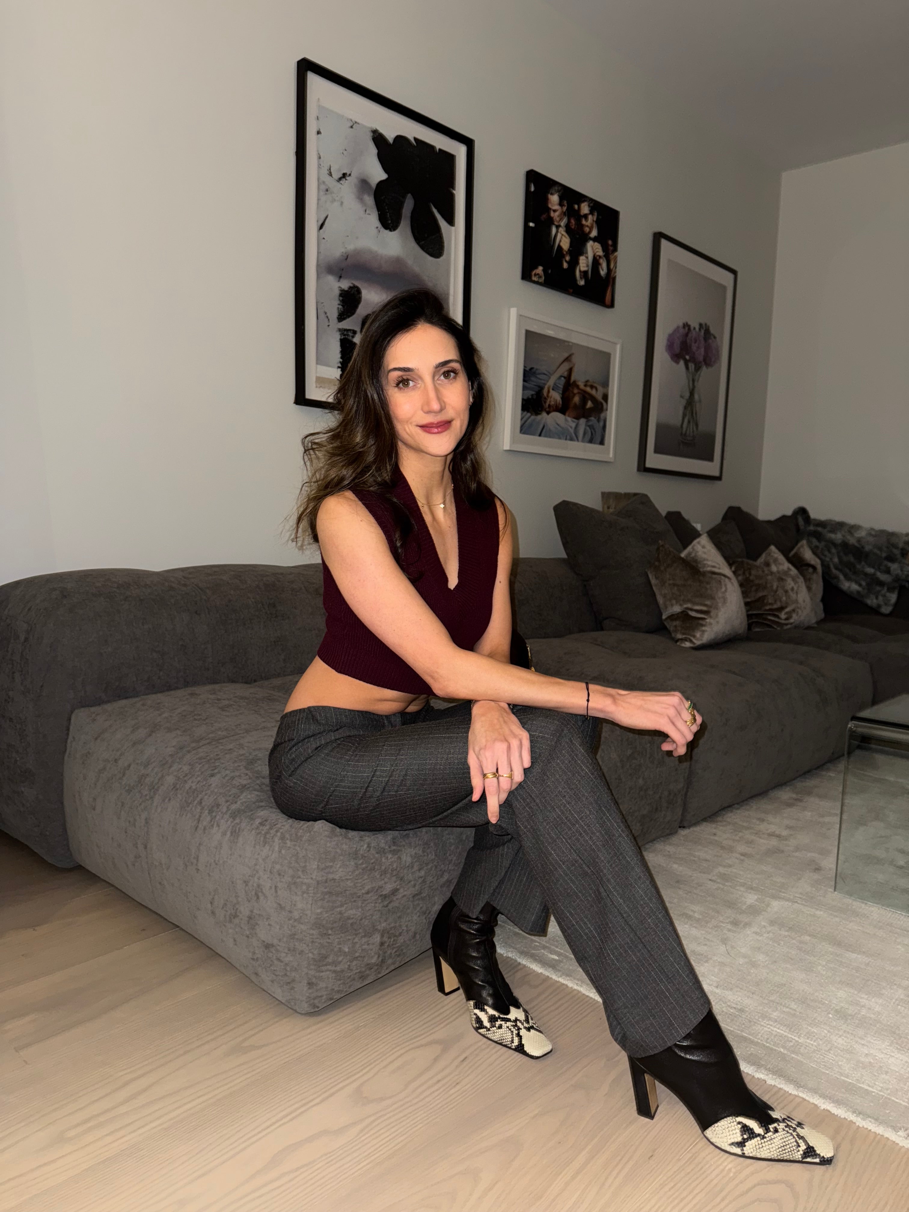 Woman sitting on a gray sofa in a room with framed pictures on the wall.
